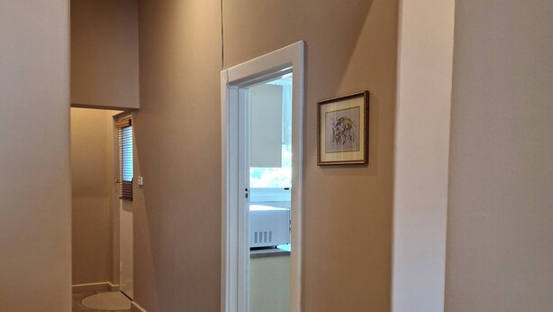 Un couloir étroit au plancher de bois, une porte blanche et un tableau encadré accroché au mur.