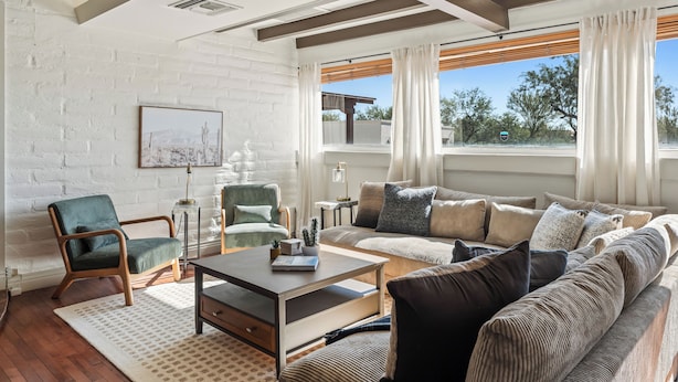 Una sala de estar moderna con pared de ladrillo blanco, vigas de madera, un sillón verde, un sofá color beige y una mesa de centro.