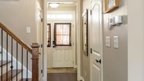 Un couloir avec un escalier en bois sur la gauche, une porte au fond et un luminaire au plafond.