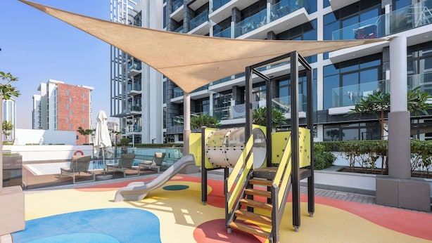 A rooftop playground with slides and climbing structures, surrounded by modern buildings and a clear sky. - Stayshort - Studio Apartment at Azizi Riviera With Balcony (Dubai)