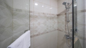A modern bathroom with a glass shower enclosure, a white towel hanging on the wall, and a patterned tile backsplash. - Stayshort - Studio Sleeps 2 in Business Bay With Canal Views (Dubai)