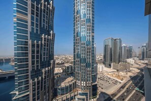 A high-rise building with a modern glass facade, surrounded by other skyscrapers and a busy road with vehicles. - Stayshort - Studio Sleeps 2 in Business Bay With Canal Views (Dubai)