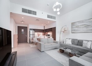 A modern living room with a grey sofa, a coffee table, and a dining area with a white table and chairs. - Stayshort - Modern Apartment Sleeps Two Dubai Creek Views (Dubai)