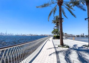 A waterfront promenade with a metal railing, palm trees, and a city skyline in the background. - Stayshort - Modern Apartment Sleeps Two Dubai Creek Views (Dubai)