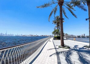 A waterfront promenade with a metal railing, palm trees, and a city skyline in the background. - Stayshort - Modern Apartment Sleeps Two Dubai Creek Views (Dubai)