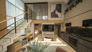 Ein modernes Interieur mit Treppe, einem Wohnbereich inklusive Sofa und Couchtisch, einer Küche mit Herd und einem Essbereich mit Tisch und Stühlen.