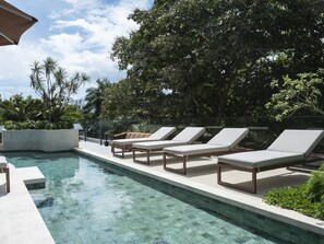 Zona de piscina con sillones reclinables y una piscina cristalina.