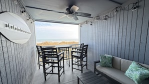 Un balcon avec vue sur la plage, aménagé avec un canapé, des chaises et une table.