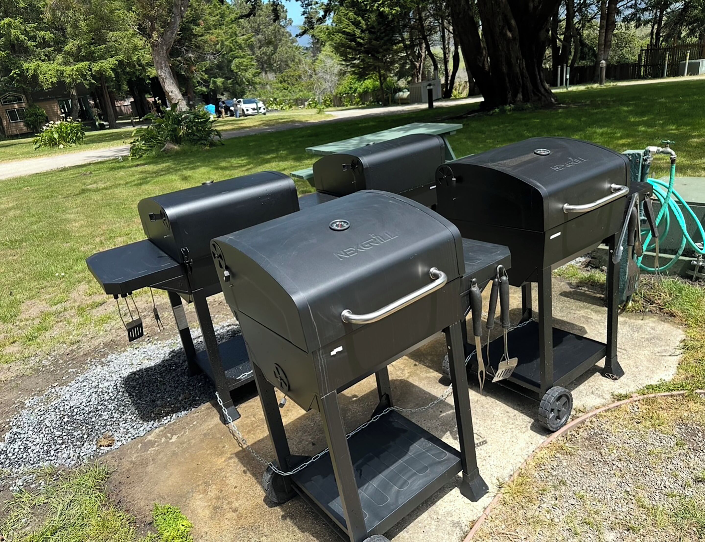 A barbecue grill set up on a concrete patio with a grassy area and trees in the background.