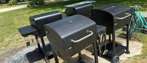 A barbecue grill set up on a concrete patio with a grassy area and trees in the background.