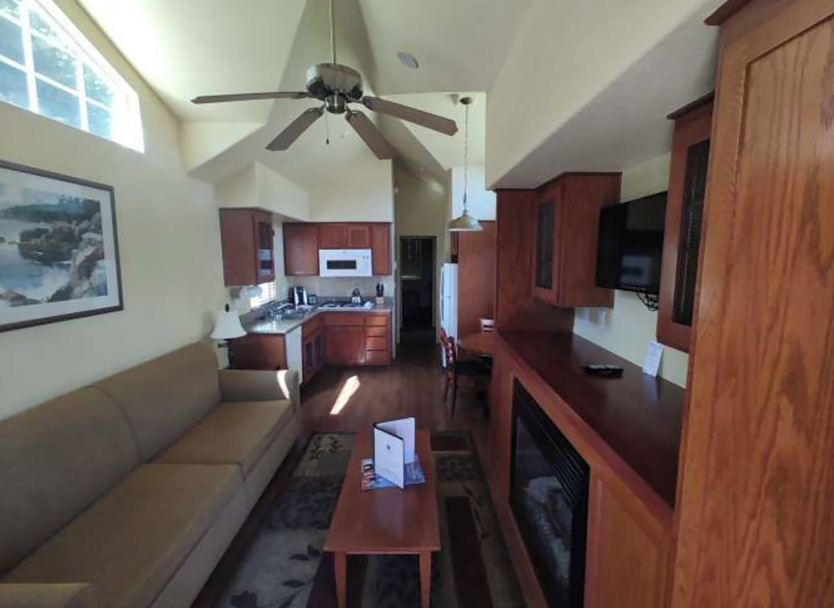 A compact living space with a kitchenette, a ceiling fan, a television, and a framed picture on the wall.
