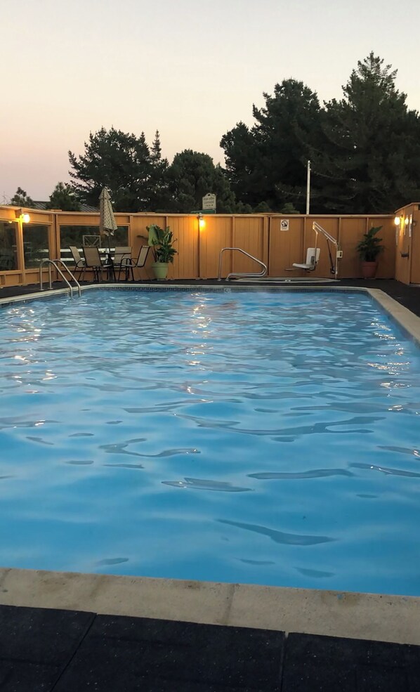 A swimming pool with a deck area, chairs, and potted plants.