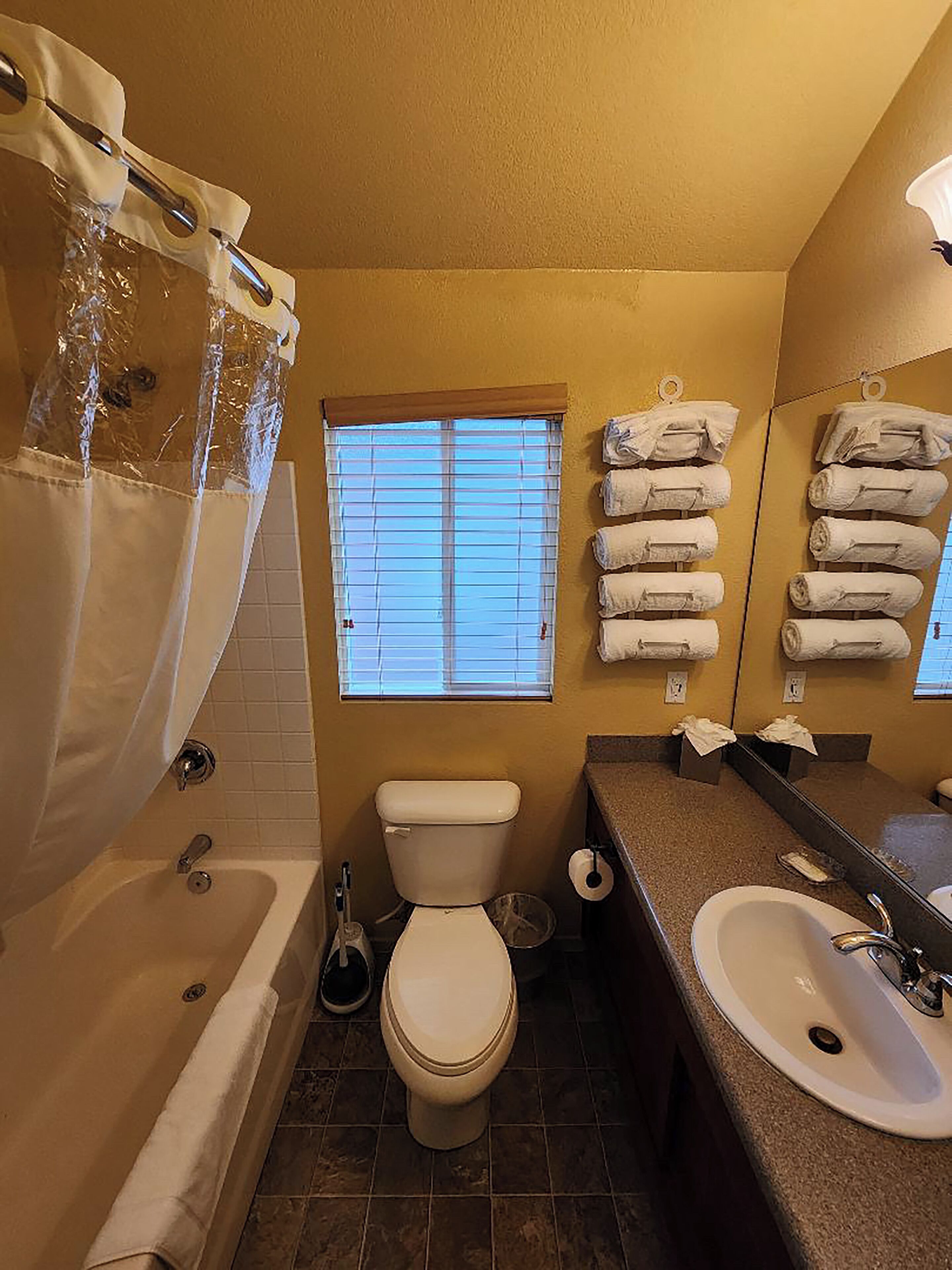 A bathroom with a bathtub, toilet, sink, and a window with blinds.