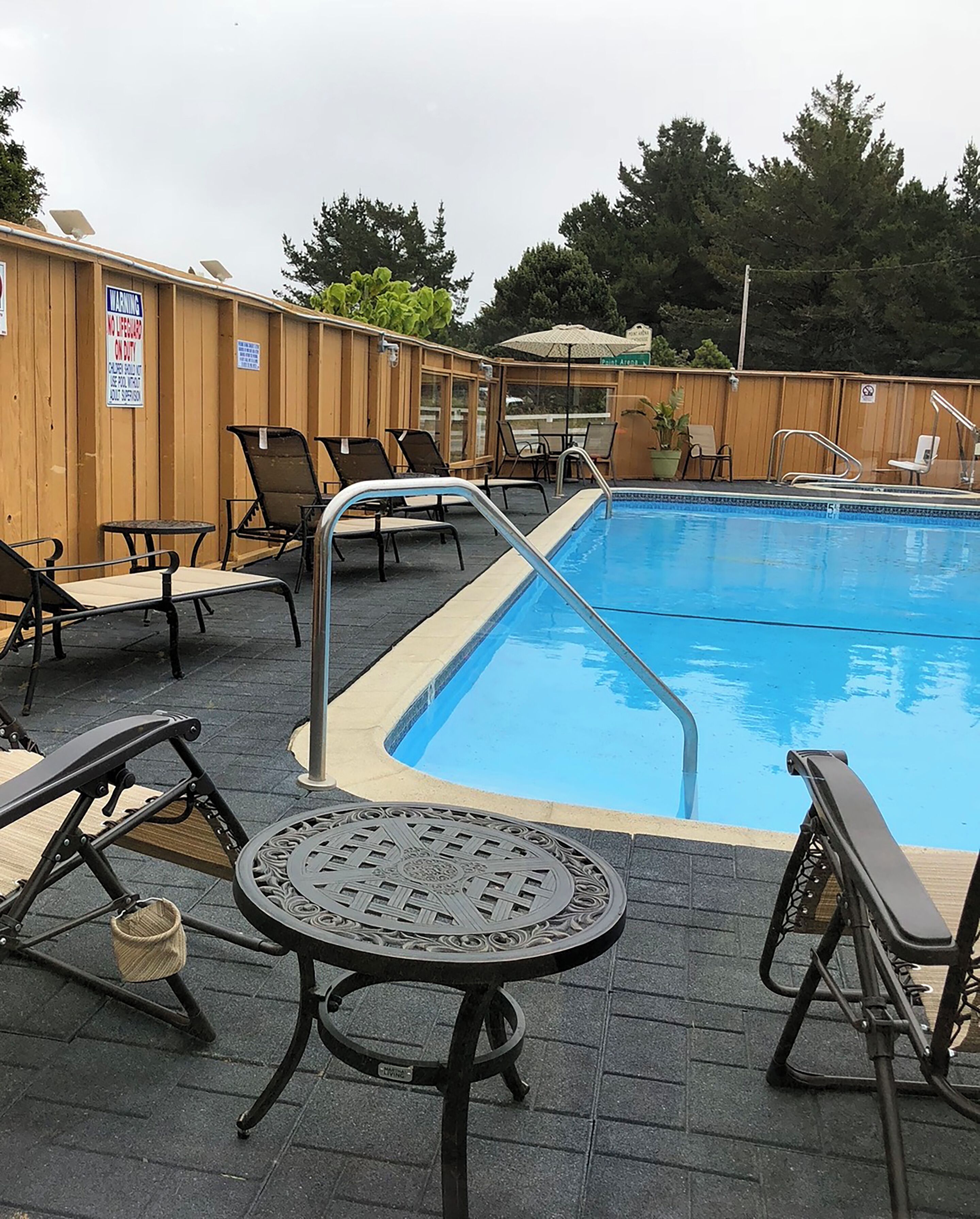 Ein Swimmingpool mit Liegestühlen und Tischen, umgeben von Holzzaun.
