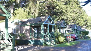 A row of cabins with green trim, wooden decks, and a gravel driveway. - Lighthouse Pointe Resort (Point Arena)