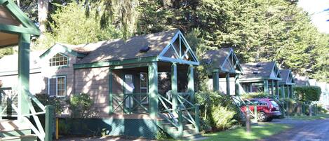 A row of cabins with green trim, wooden decks, and a gravel driveway.