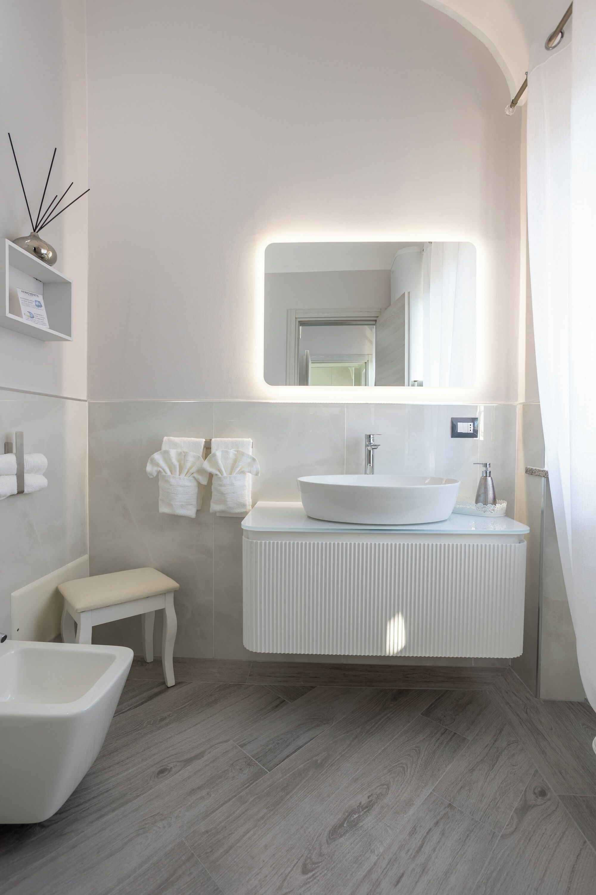 A modern bathroom with a large white sink, a mirror, and a bench.