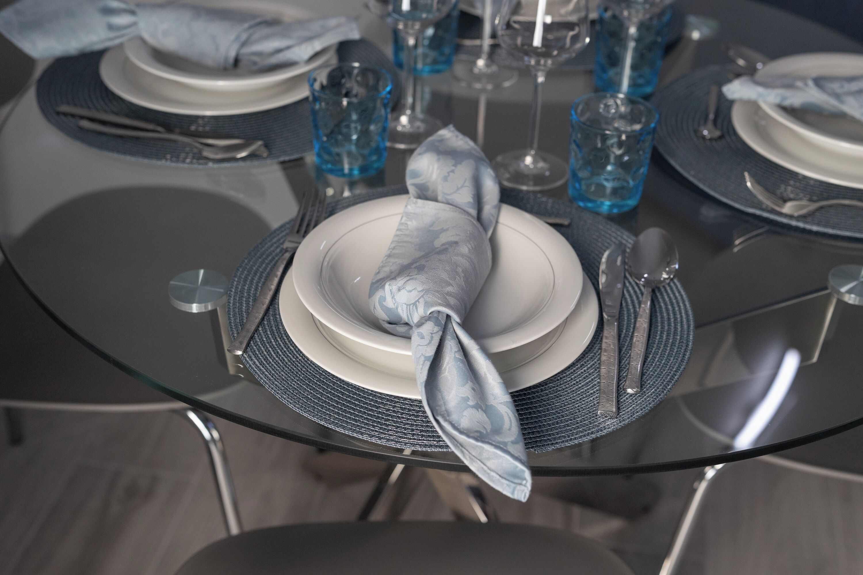 A table set for a formal meal with plates, cutlery, and blue glassware.