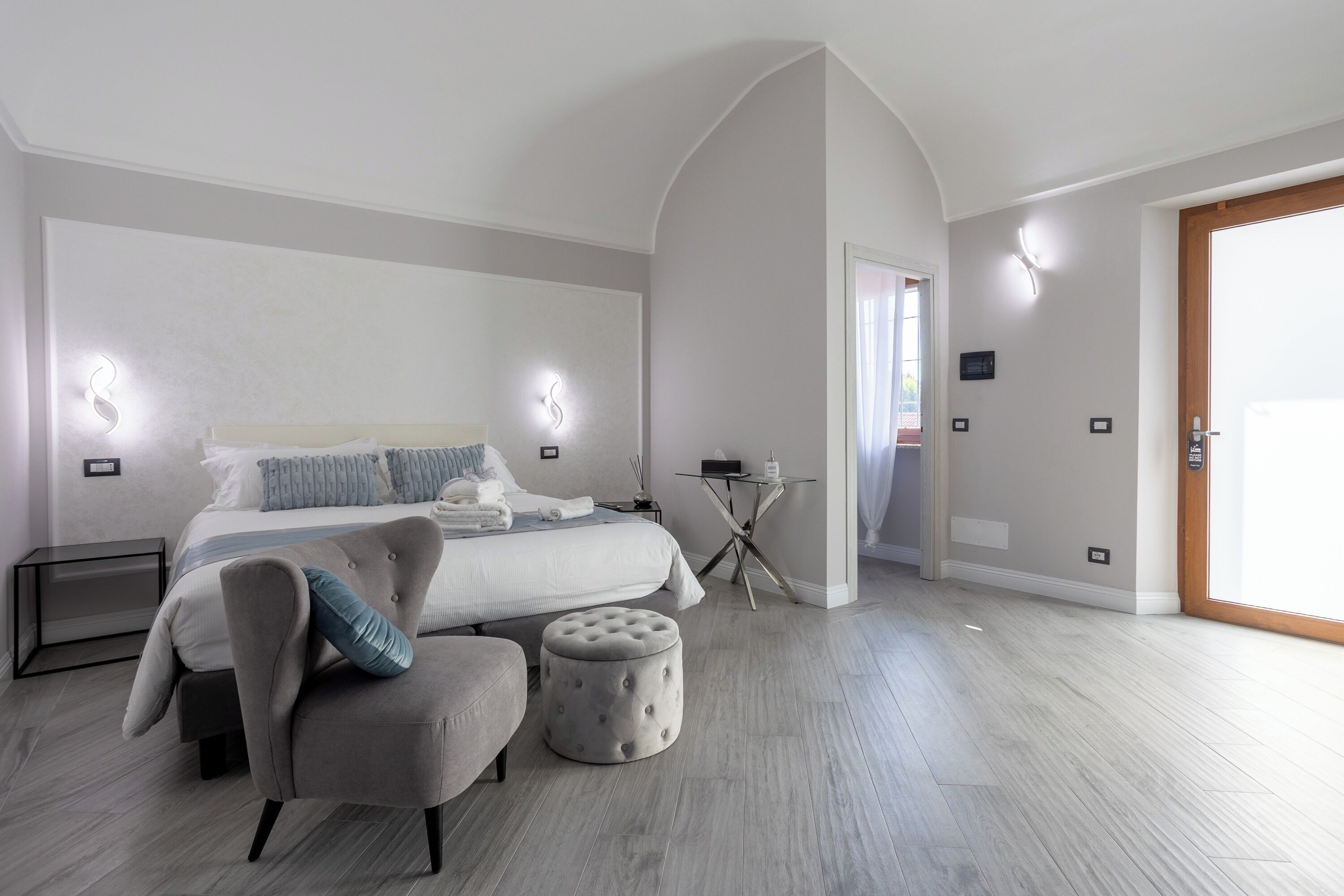 Une chambre à coucher moderne comprenant un lit, une chaise, un petit pouf, une table de chevet et un bureau avec une chaise.