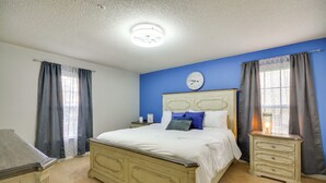 Quarto com cama, mesas de cabeceira, penteadeira e relógio de parede.