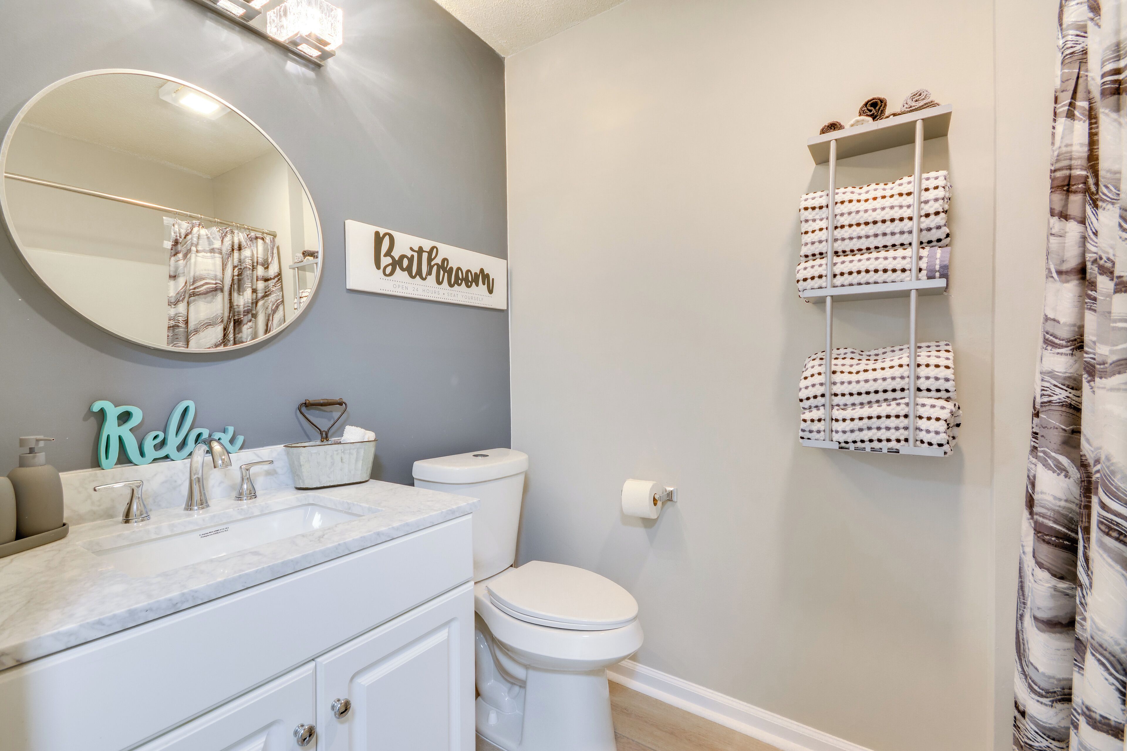 A bathroom with a marble sink, a toilet, a mirror, and shelves with towels.