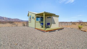 A small, single-story building with a porch and two chairs, set against a desert landscape with mountains in the background. - Tiny Town Cottages in Rodeo! 'Dog House' (Rodeo)