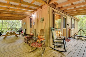 Una terraza de madera con mesas de picnic y mecedoras, rodeada de paredes de madera y ventanas amplias.