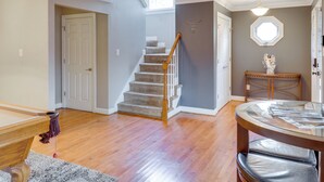 A spacious room with hardwood flooring, a staircase, a dining area with a round table, and a decorative wall piece. - Centrally Located Hampton Roads Home w/ Game Room! (Portsmouth)