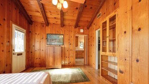 Interior de una cabaña de madera con una cama, un cuadro y un armario de madera.
