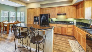 A kitchen with wooden cabinets, a black refrigerator, a stove, and two bar stools. - Napa Nearby! Large Home w/ Hot Tub & Dtwn Access (Suisun City)