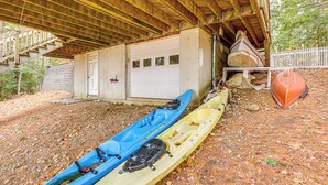 Un garage coperto con due kayak, una canoa e una barca sotto un tetto di legno.