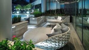 Un área lounge moderna al aire libre con una silla colgante, asientos y una piscina al fondo.