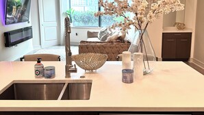 Una cocina moderna con un lavaplatos de acero inoxidable, horno empotrado y lavavajillas. Hay un amplio ventanal con vistas a la ciudad.