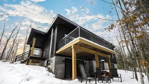 Une maison de campagne moderne à deux étages, dotée d’un balcon, d’une cheminée et d’une terrasse.
