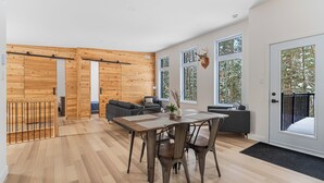 Un vaste espace de vie doté d’un plancher en bois, d’une table à manger avec des chaises, d’un canapé et d’une grande fenêtre ornée d’une tête de cerf.