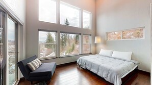 Un dormitorio con cama, sofá y varias ventanas que ofrecen vistas a árboles y un paisaje urbano.