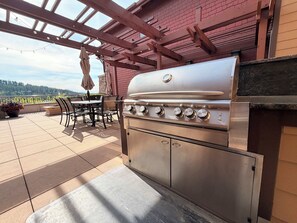 A patio with a stainless steel grill, outdoor furniture, and a brick wall. - Walkable Getaway – 2BR Steps from Dining & Trails (Coeur d'Alene)