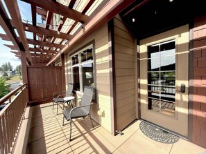 Un balcón cubierto con dos sillas y una mesa, barandillas de madera y vistas al exterior.