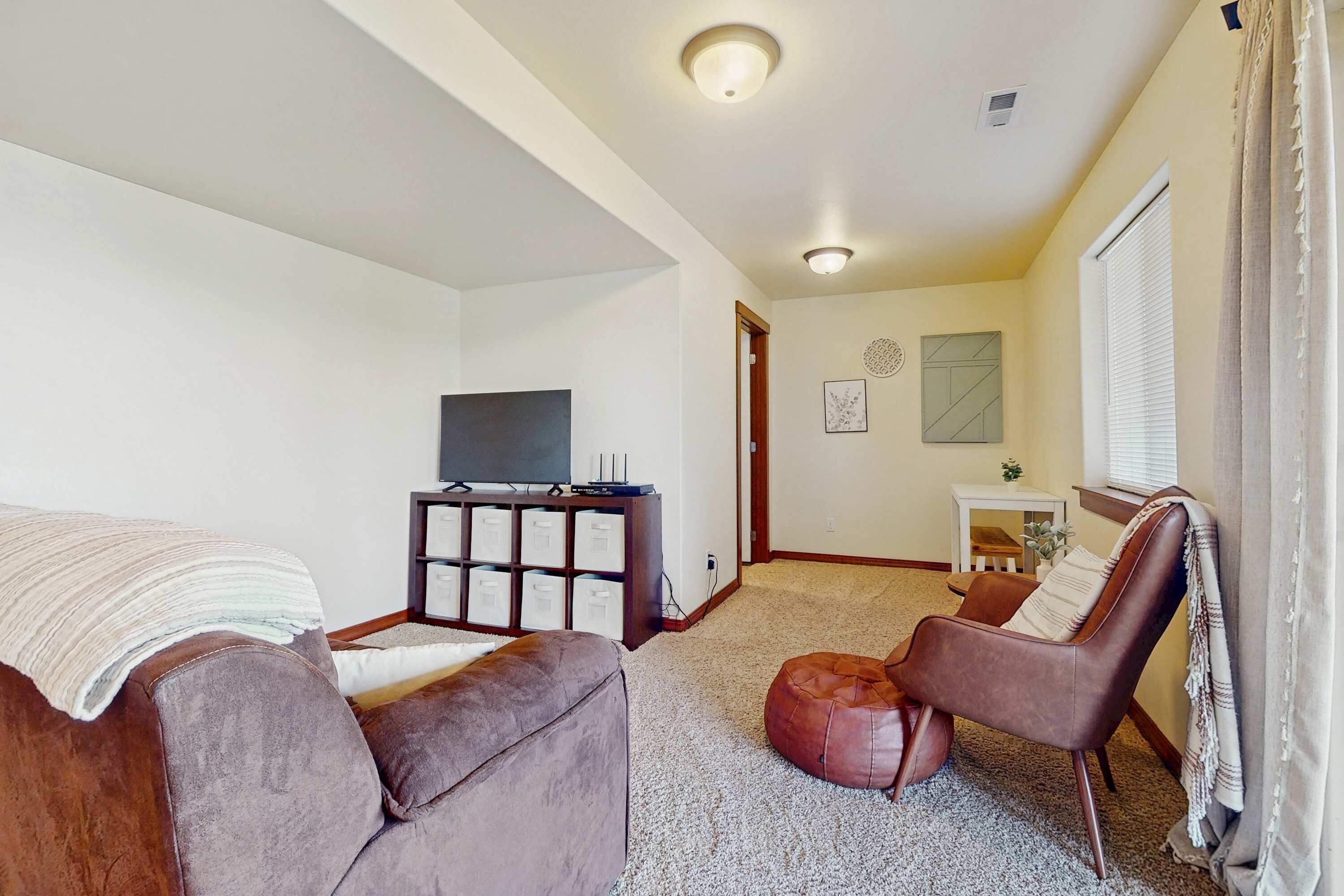 A modern hotel room with a large bed, a brown leather armchair, a small ottoman, a TV, and a cabinet.