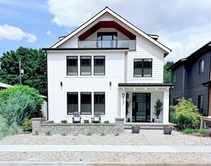 Ein zweistöckiges Haus mit Veranda, Garage und einem kleinen Garten mit Pflastersteinen.