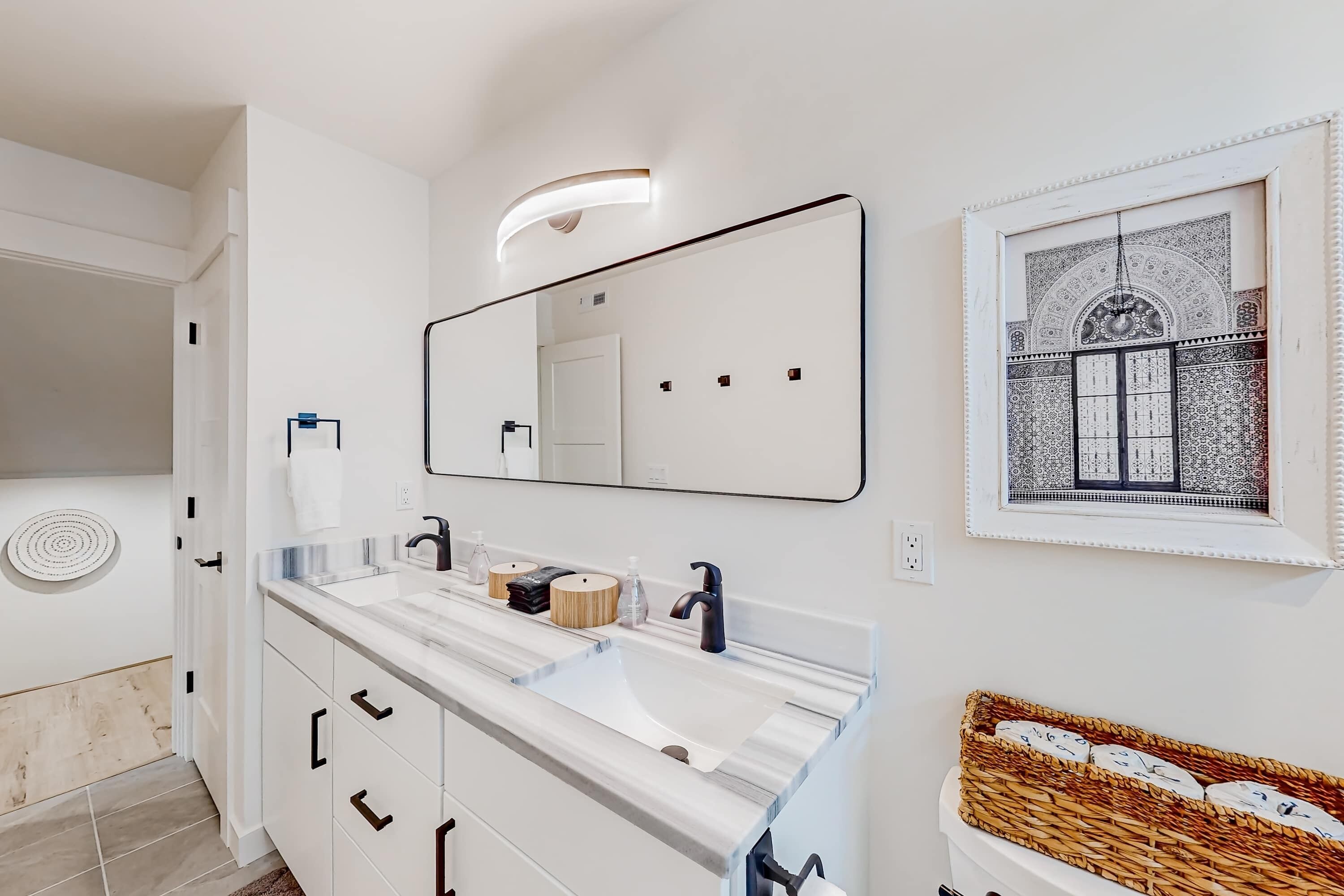A modern bathroom with a large mirror, two sinks, and a decorative wall piece.