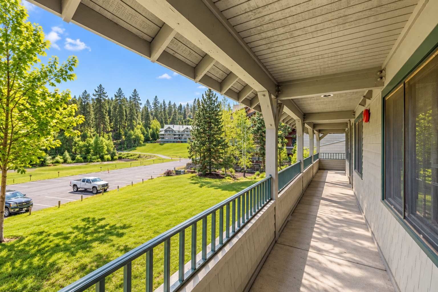 A covered balcony with a view of a parking lot and a building in the distance.