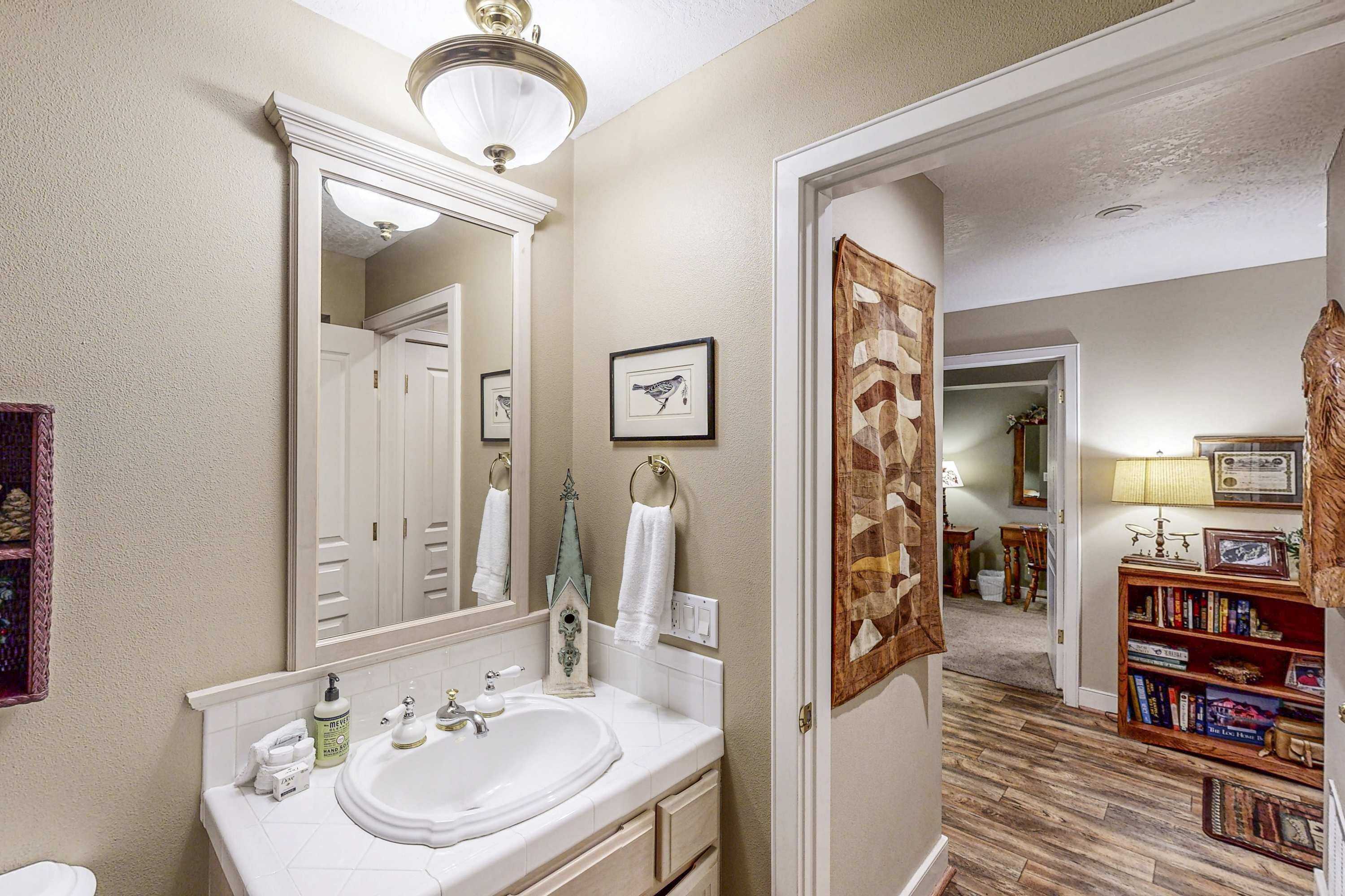 Une salle de bain avec un grand miroir, un lavabo blanc et un plancher en bois.
