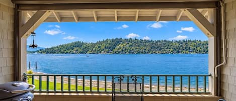 Un espacio al aire libre techado con vista a un lago, una parrilla y una mesa con sillas.