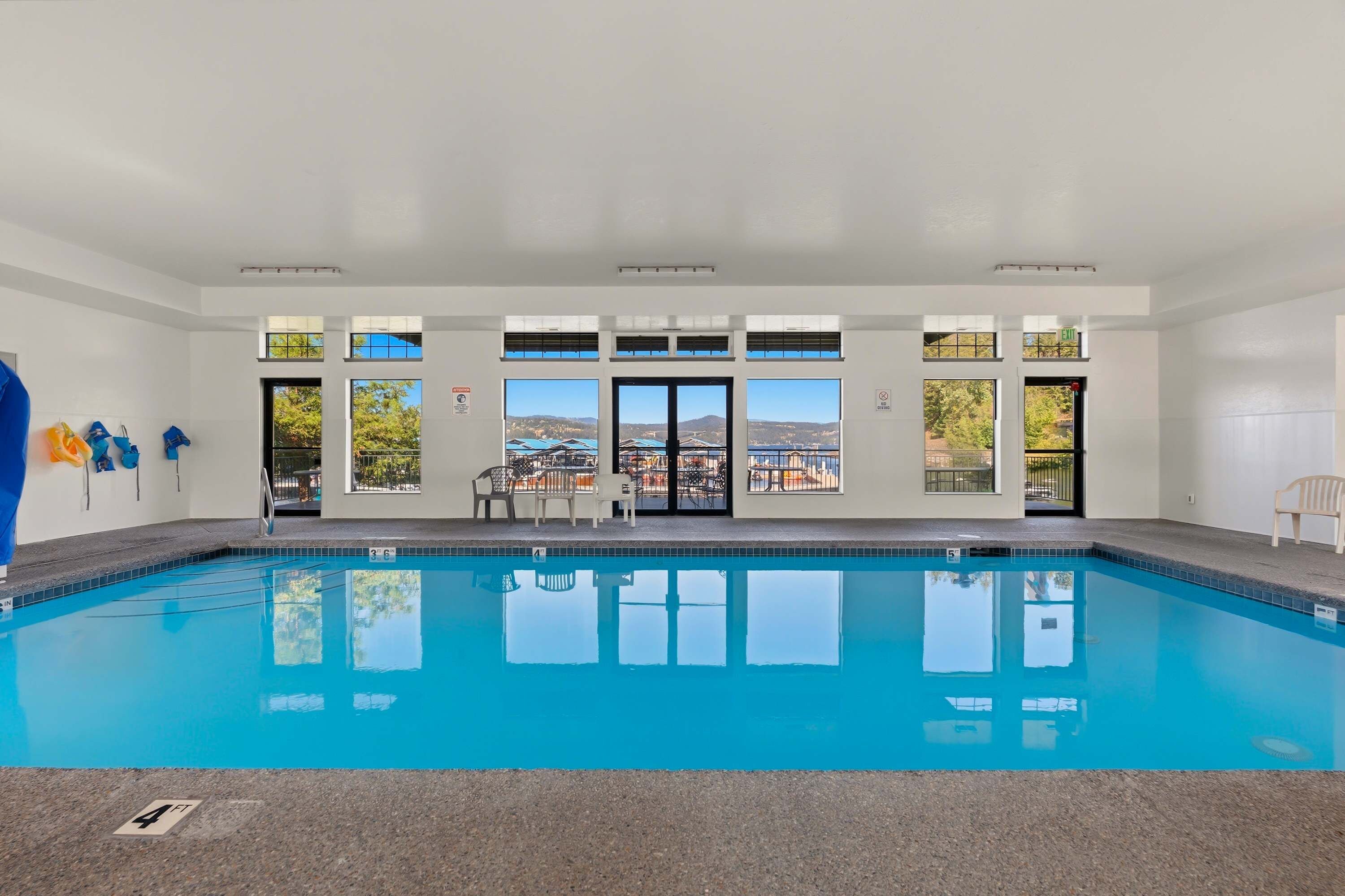 A swimming pool with clear blue water, surrounded by a white interior with multiple windows offering views of the outdoors.