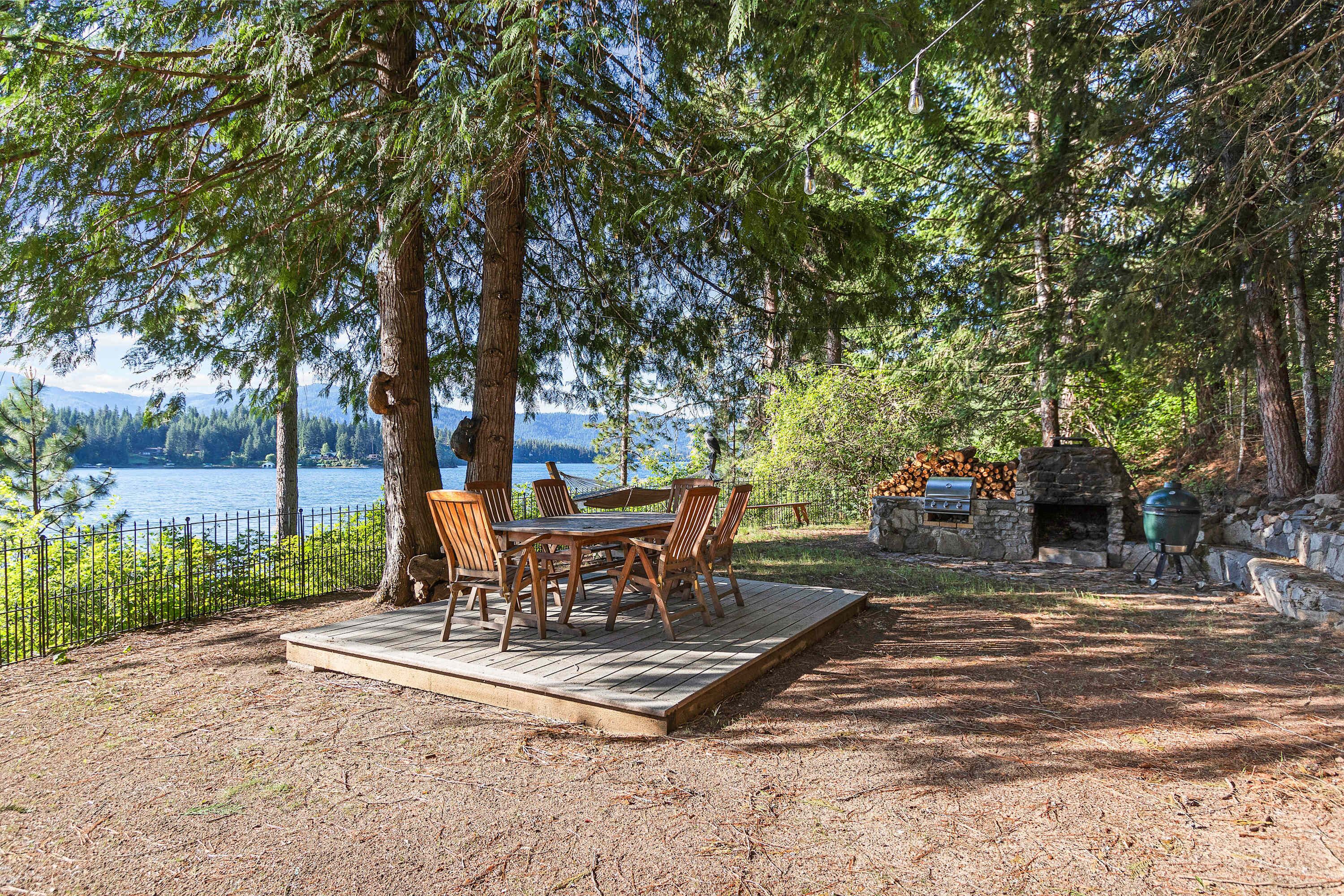 Een terras met tafel en stoelen met uitzicht op een meer, omringd door bomen.