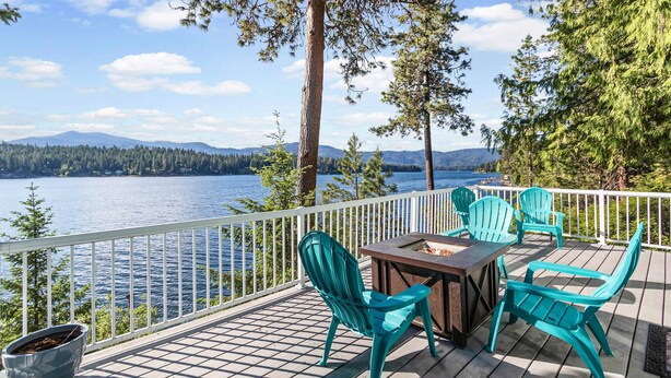 A deck with a table and chairs, overlooking a lake with mountains in the background.