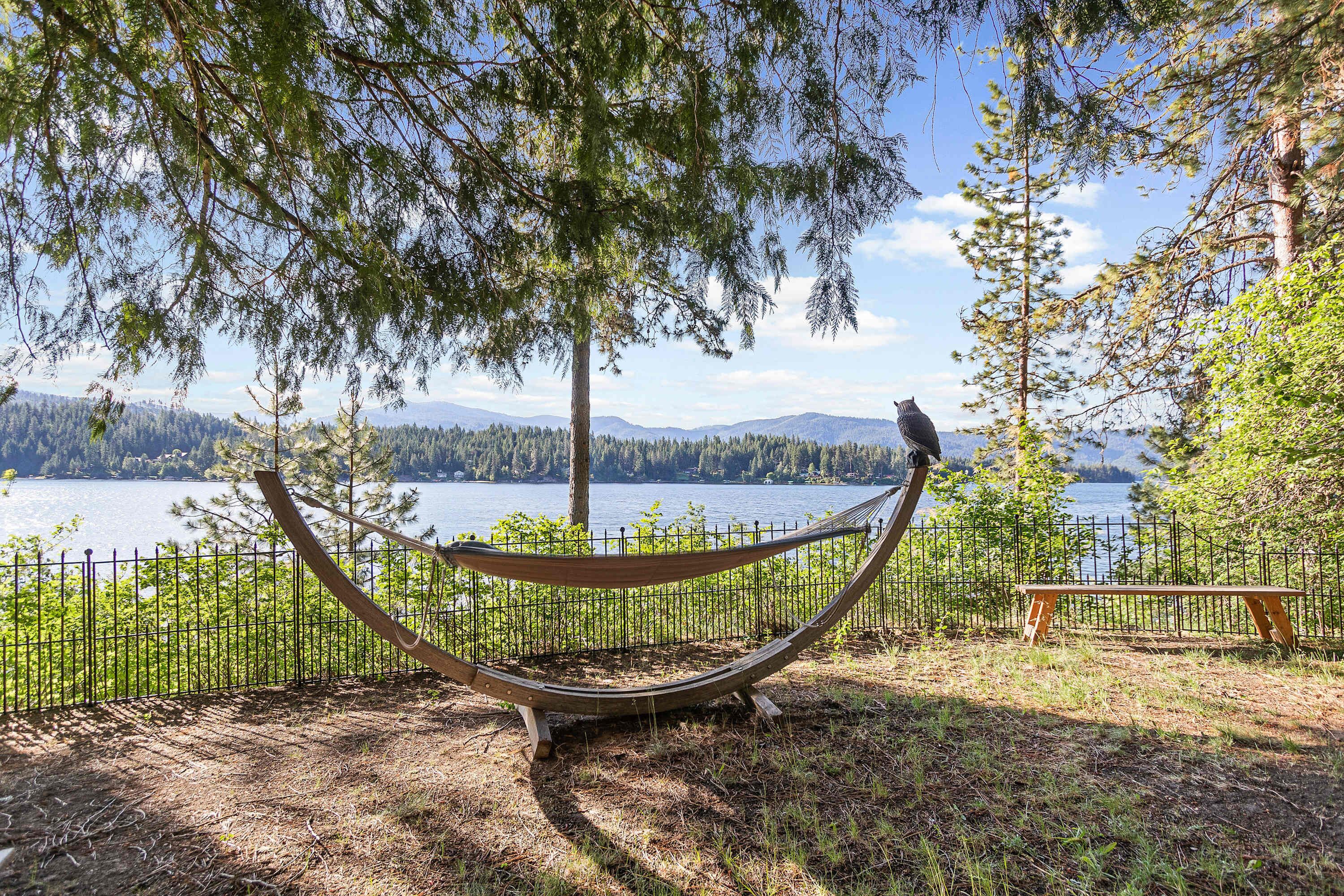 A hammock with a bird perched on it, overlooking a lake and forested mountains.