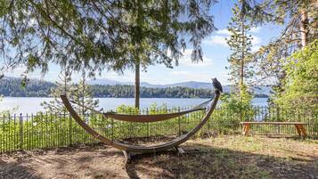 A hammock with a bird perched on it, overlooking a lake and forested mountains.