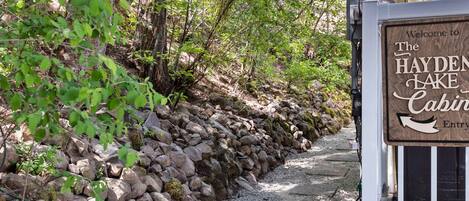 A stone pathway leading to a cabin entrance with a sign reading "Welcome to The Hayden Lake Cabin Entry".